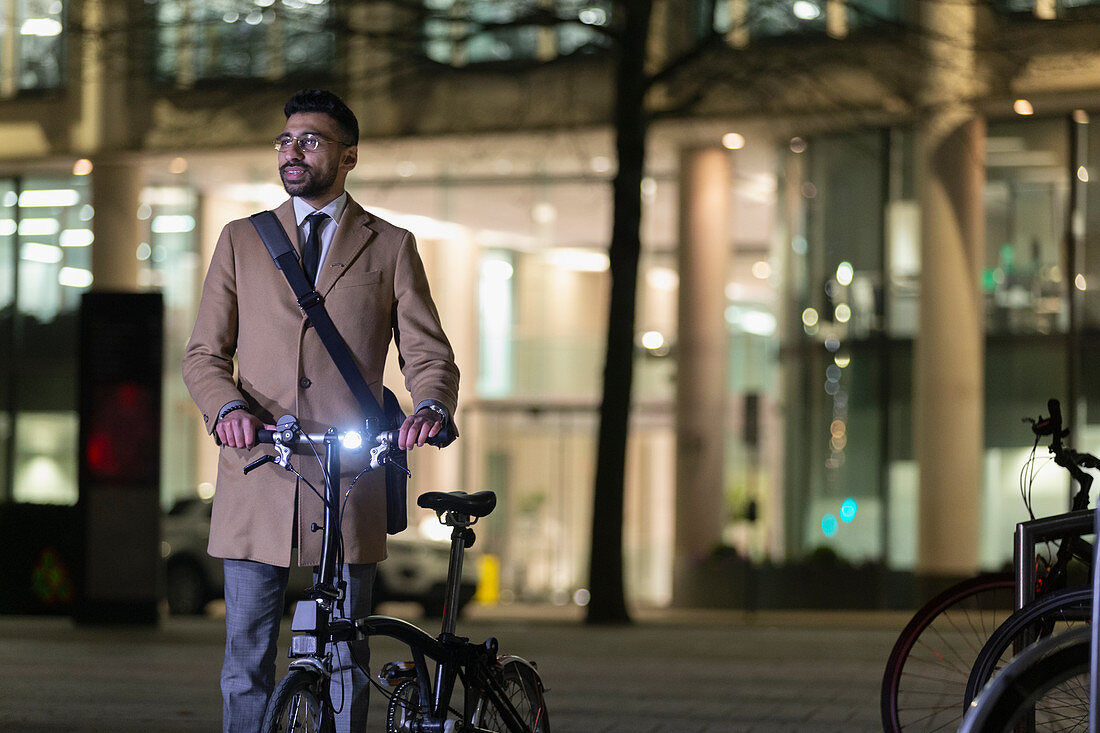 Businessman with bicycle on urban street at night