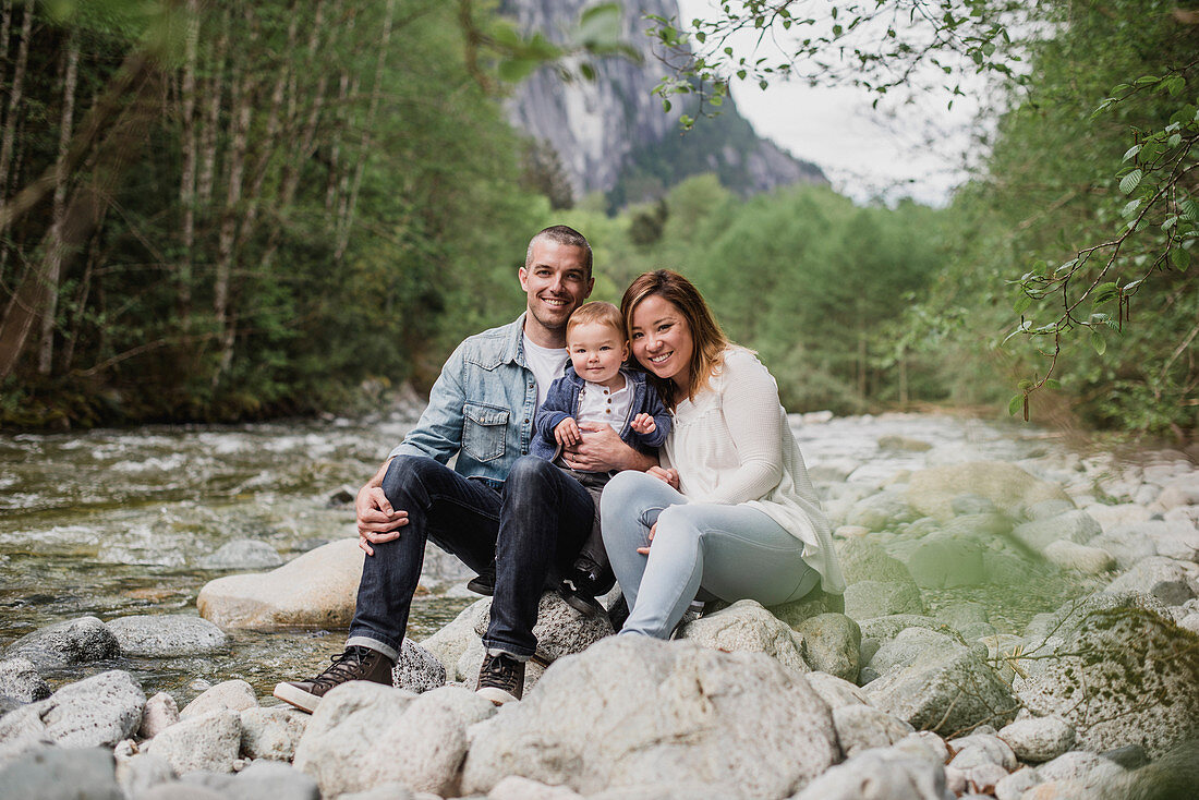 Parents and baby son sitting on rocks at riverside