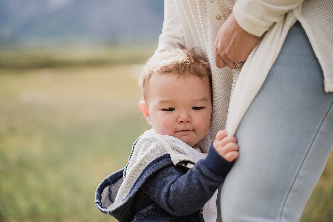 Affectionate baby son clinging to mother's legs