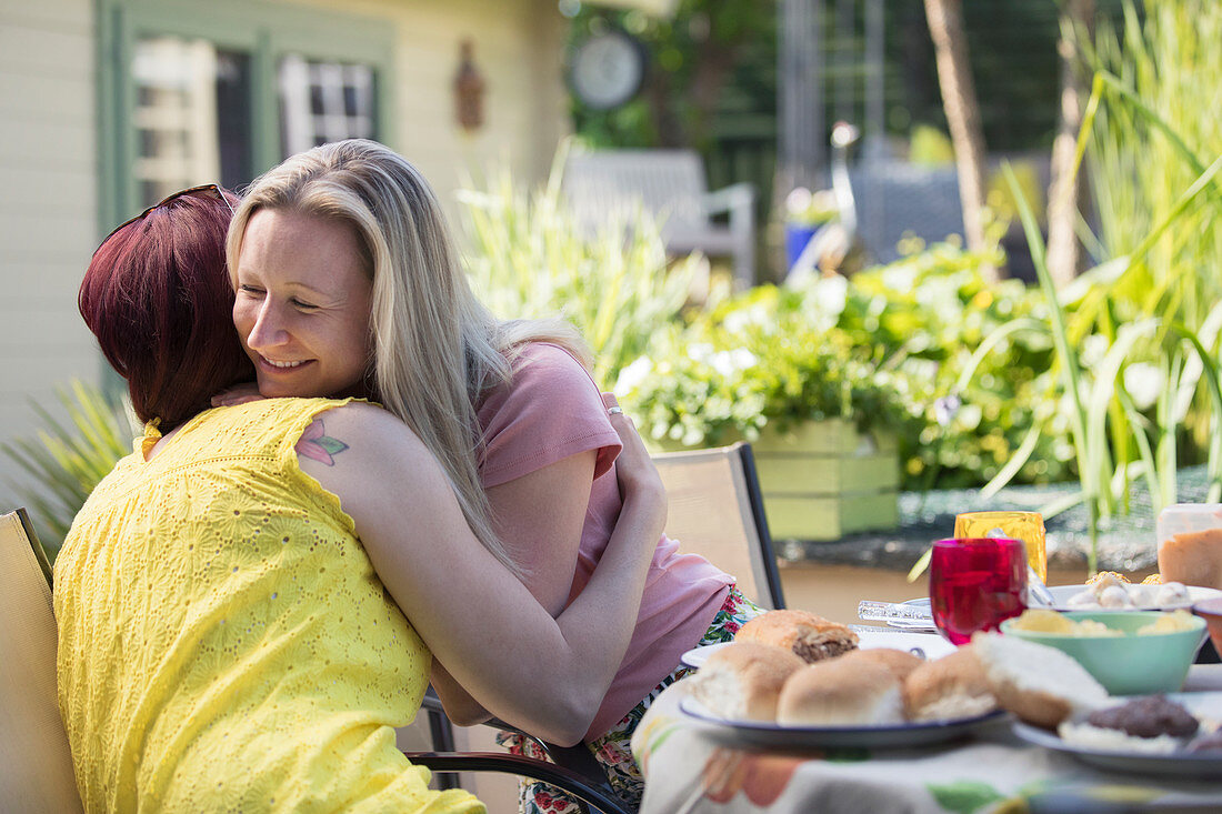 Lesbian couple hugging at lunch patio table