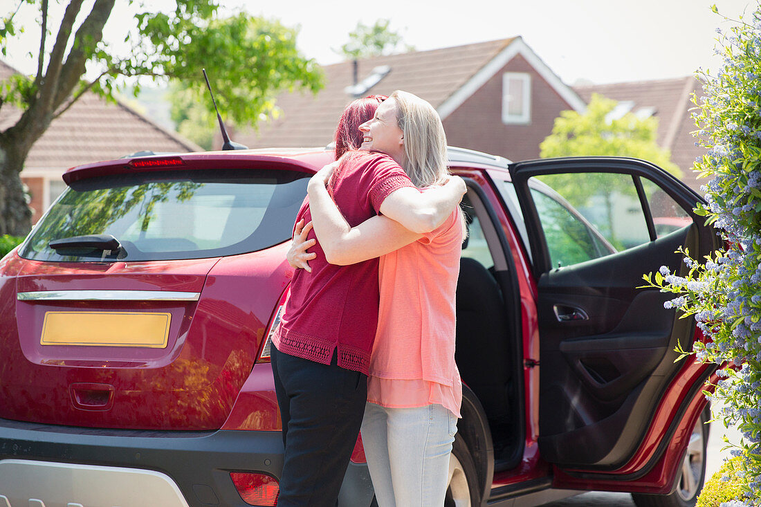 Lesbian couple hugging by car in sunny driveway