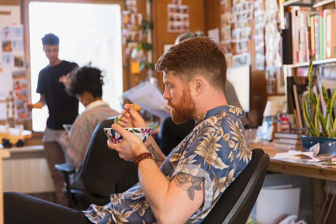 Creative businessman eating soup in office