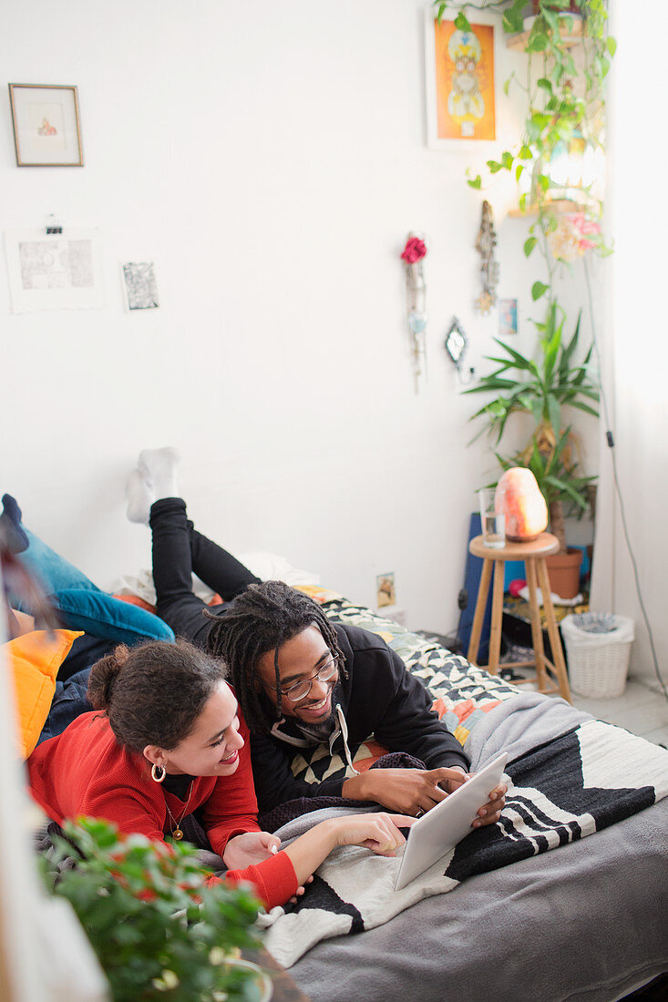 Young couple relaxing, using digital tablet on bed