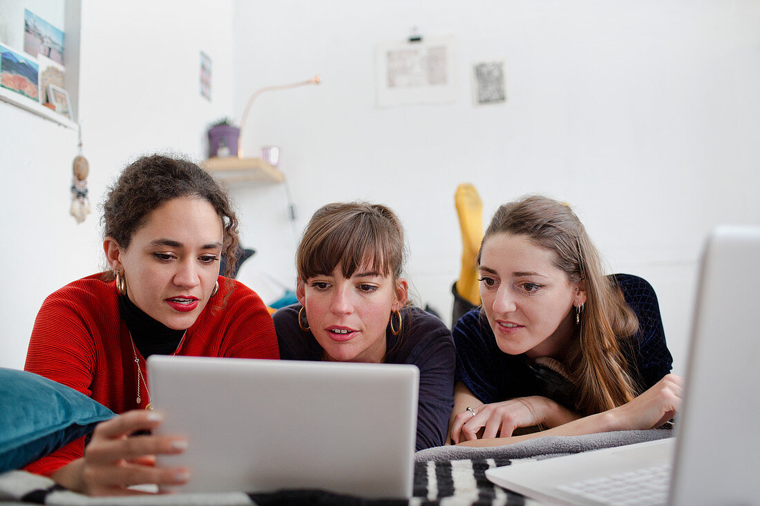 Young women friends sharing digital tablet on bed