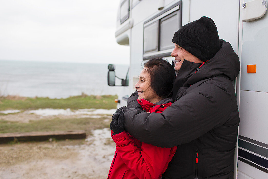 Couple in warm clothing hugging outside motor home