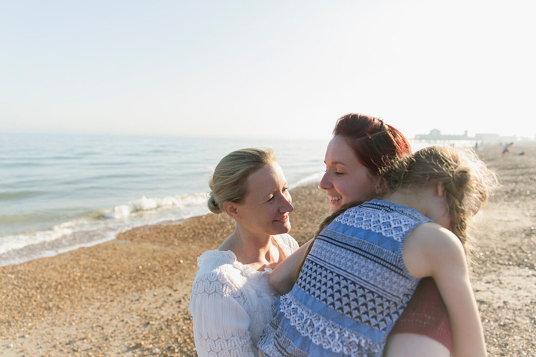 Lesbian couple hugging daughter on beach