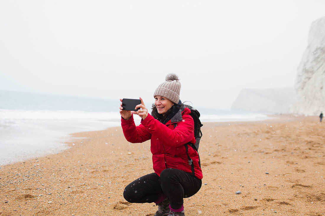 Woman using camera phone on snowy beach