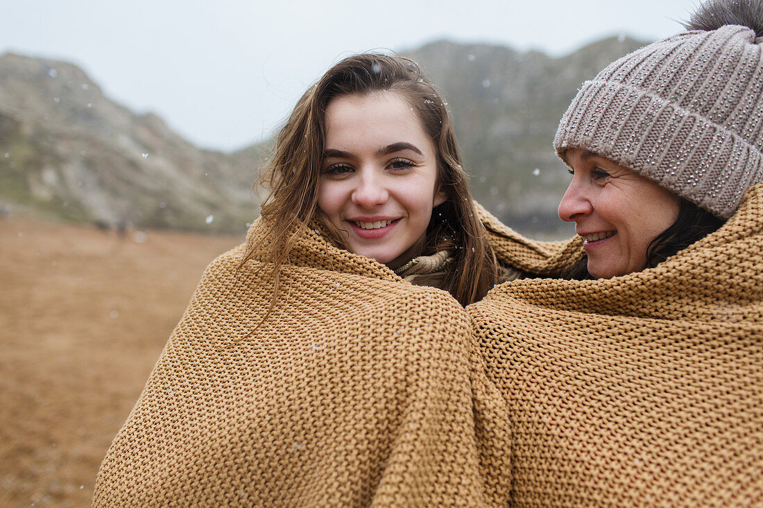 Mother and daughter wrapped in a blanket on beach