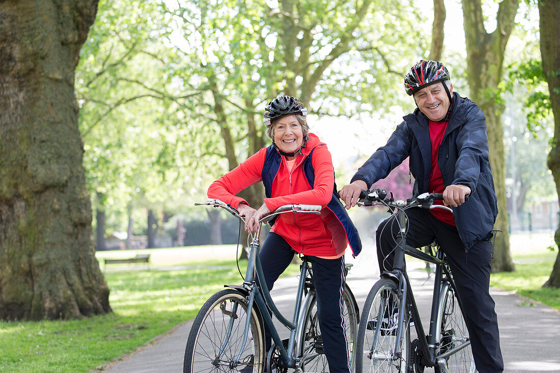 Portrait active senior couple riding bikes in park