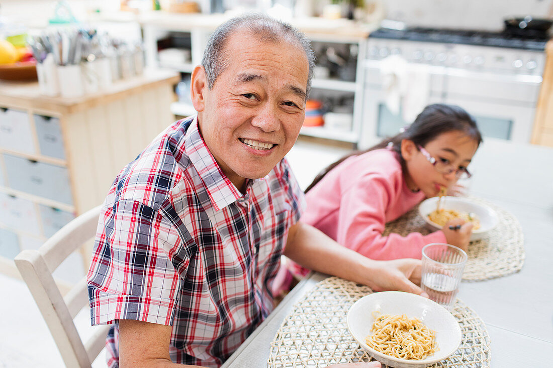 Grandfather eating noodles with granddaughter