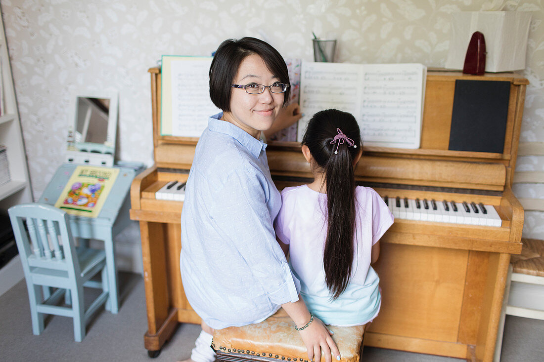 Mother sitting with daughter playing piano