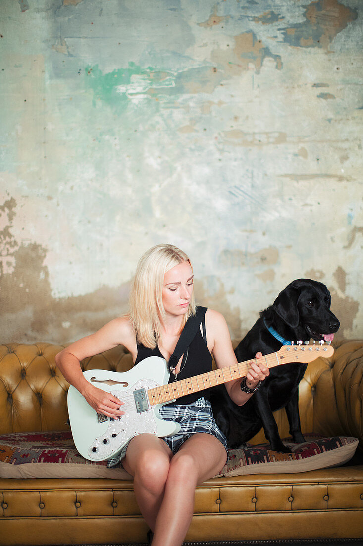 Young woman with dog playing electric guitar