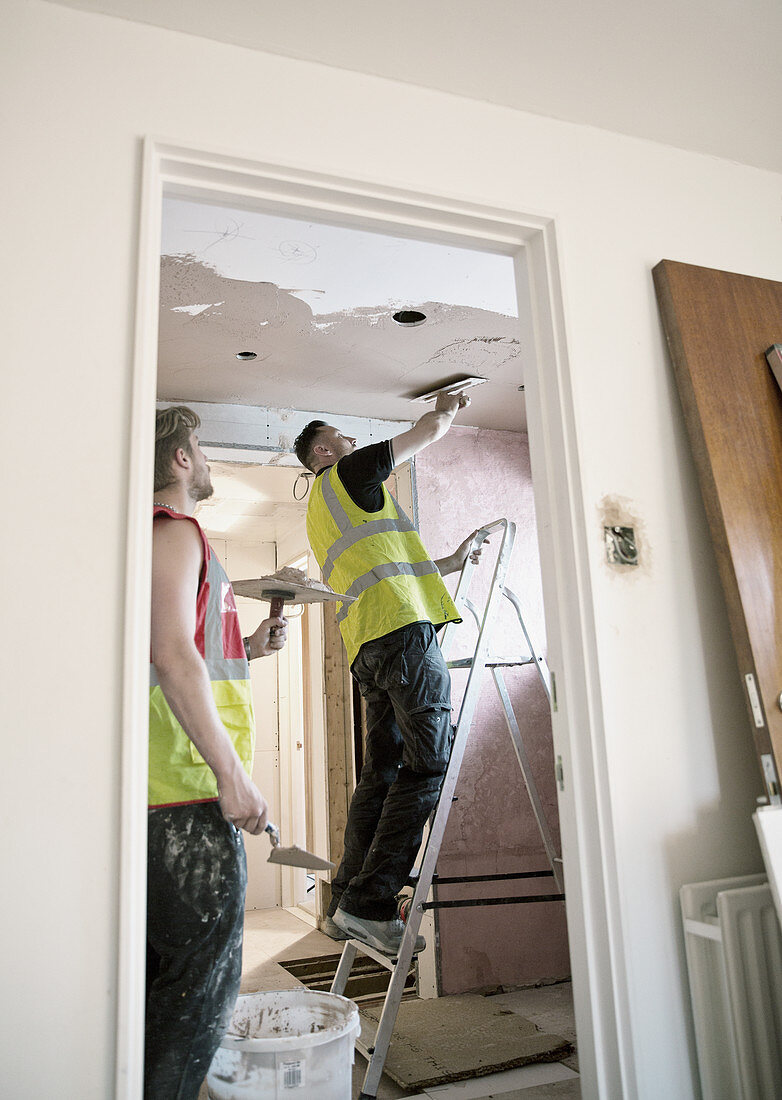 Construction workers plastering ceiling in house