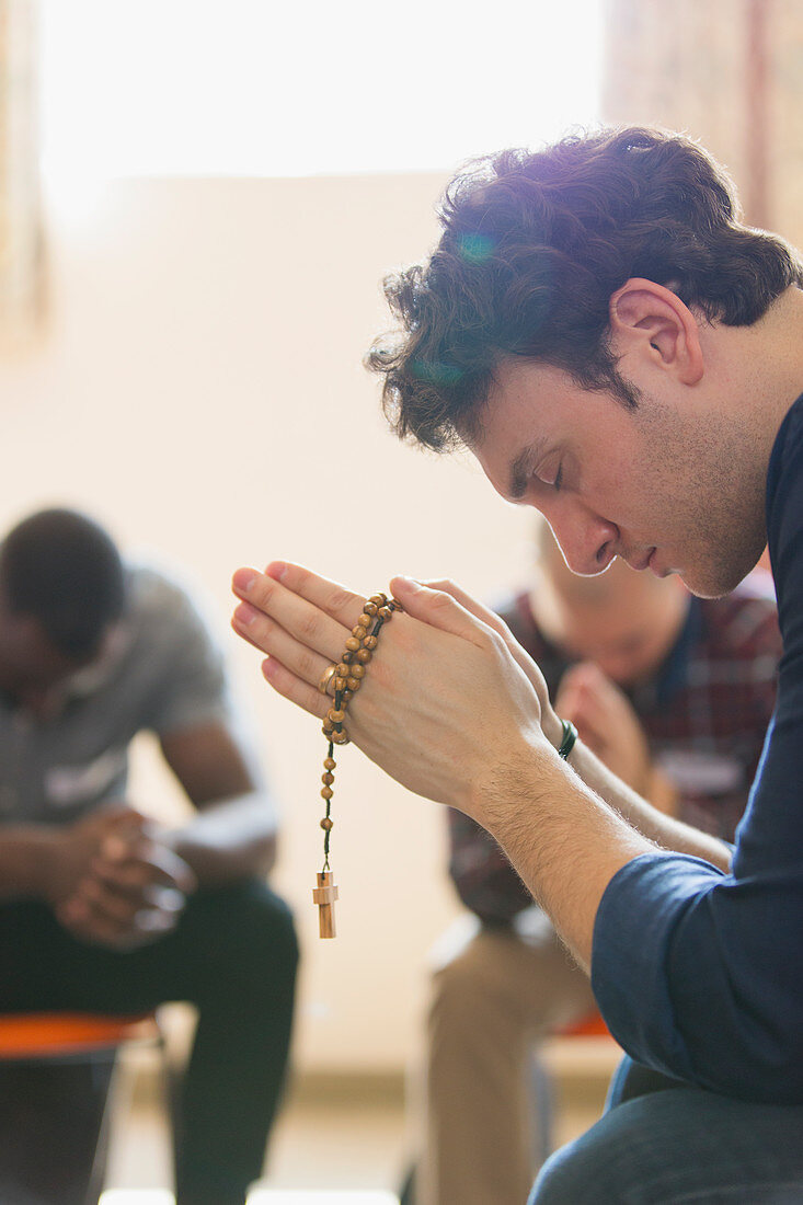 Serene man praying with rosary in prayer group