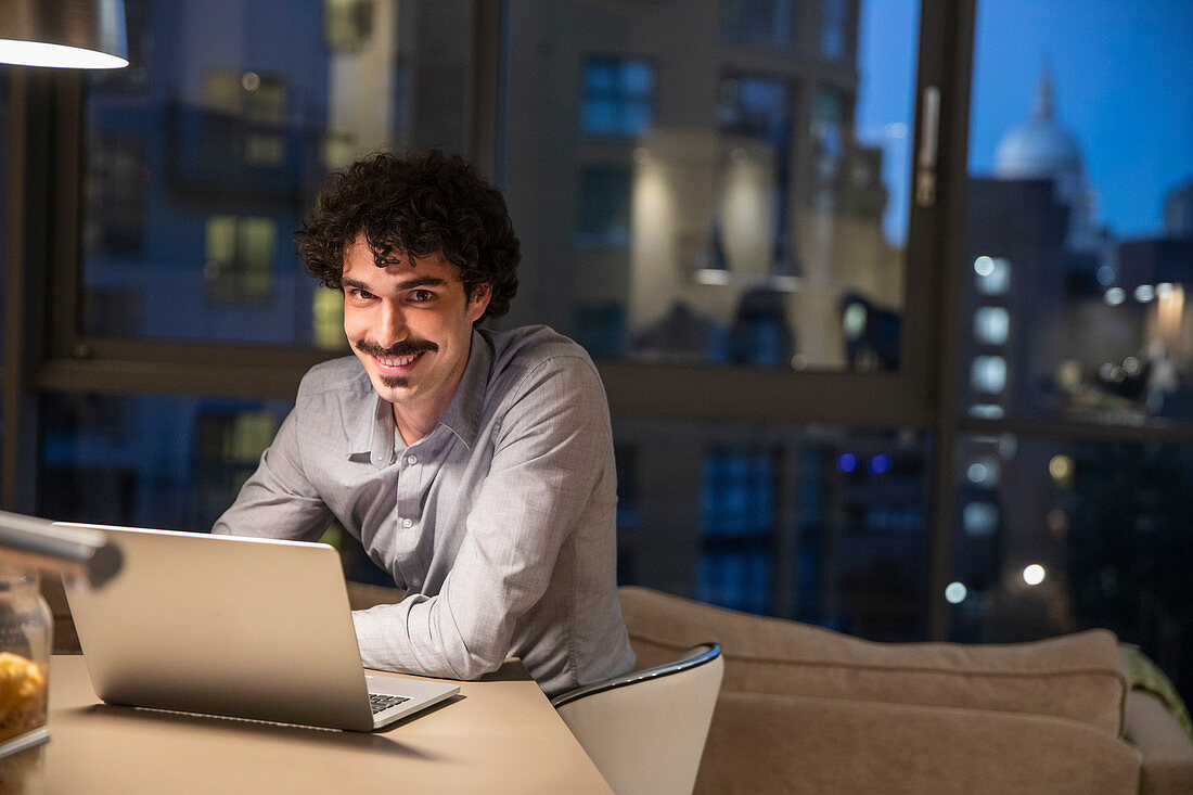 Portrait smiling man using laptop at night