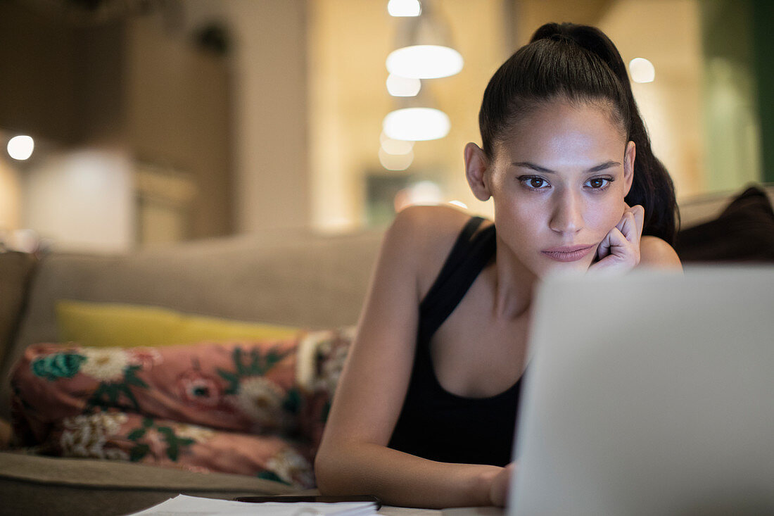 Focused woman in pyjamas using laptop on sofa