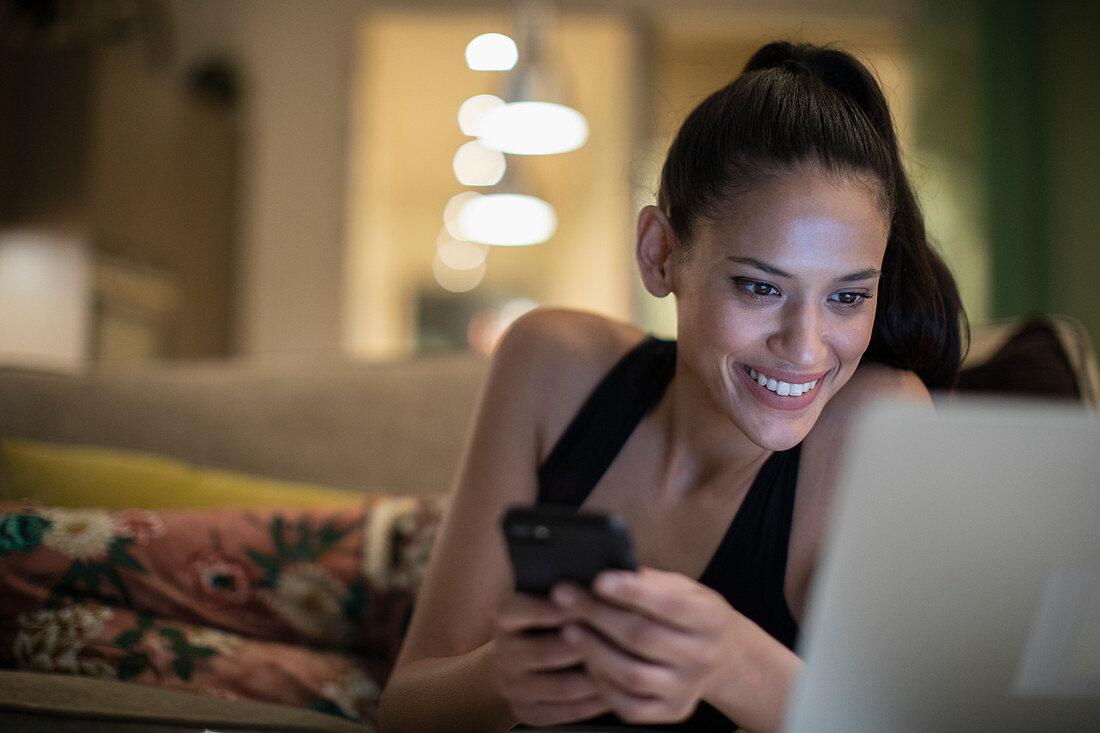 Woman in pyjamas using smart phone and laptop