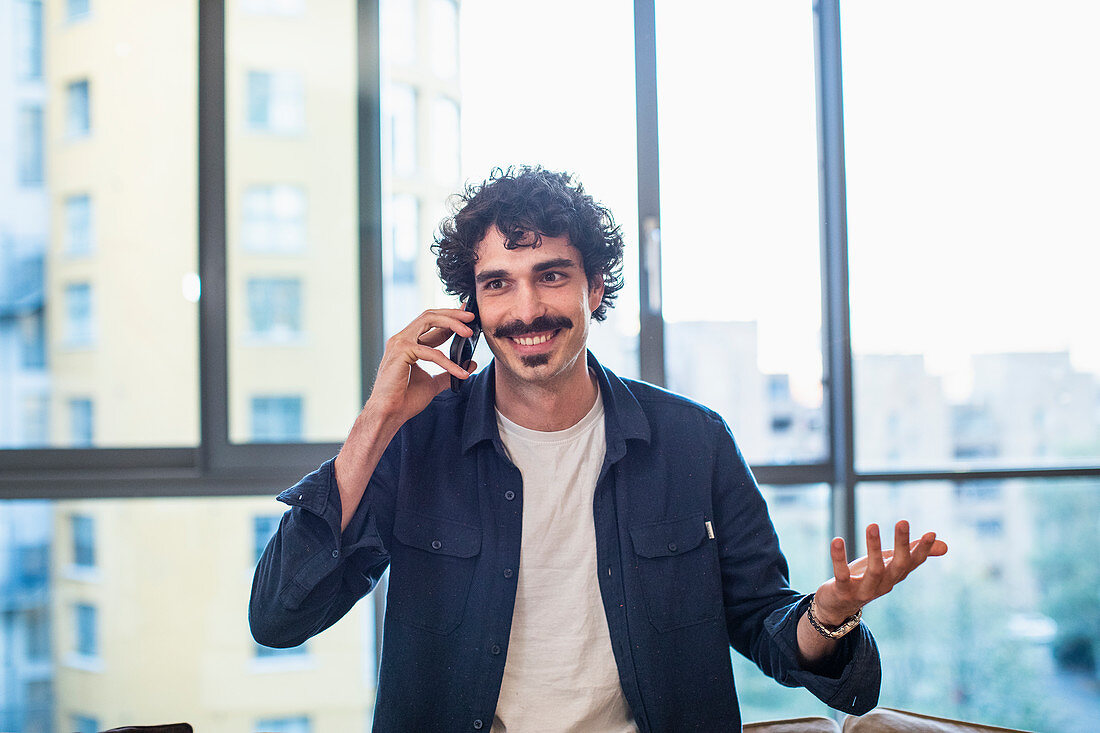Smiling man talking on smart phone in urban apartment