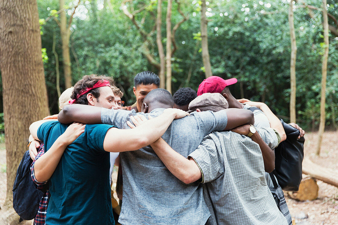 Men friends hugging in huddle on hike in woods