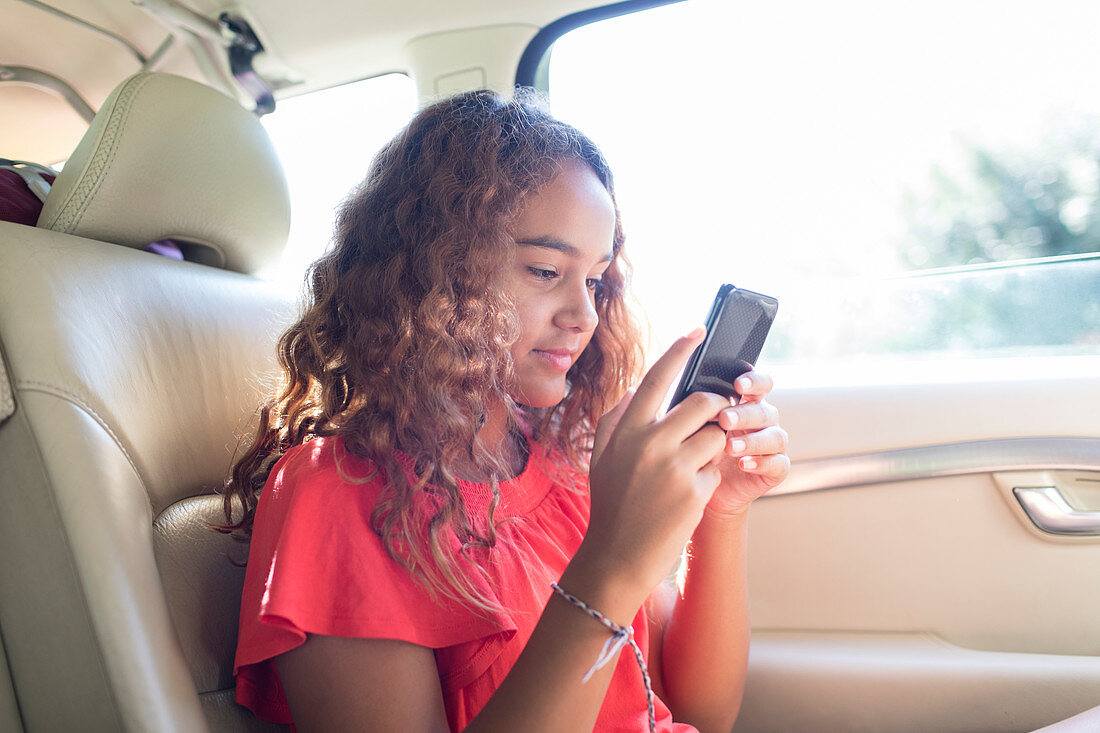 Tween girl using smart phone in back seat of car