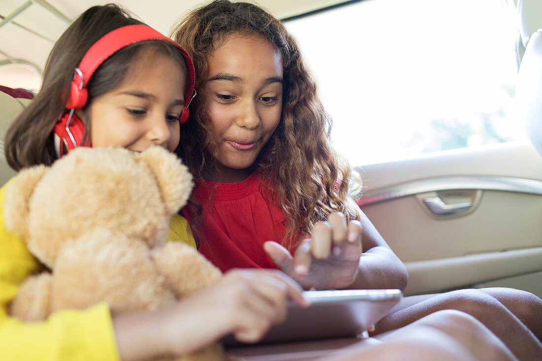 Sisters using tablet in back seat of car