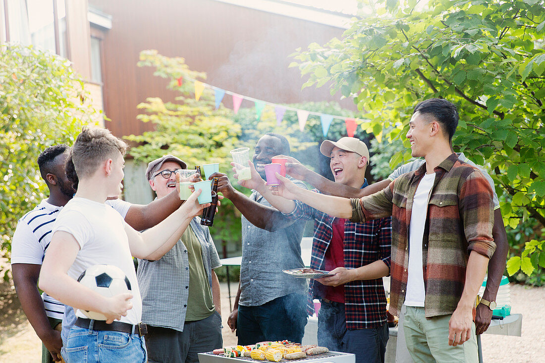 Happy male friends toasting drinks over barbecue grill