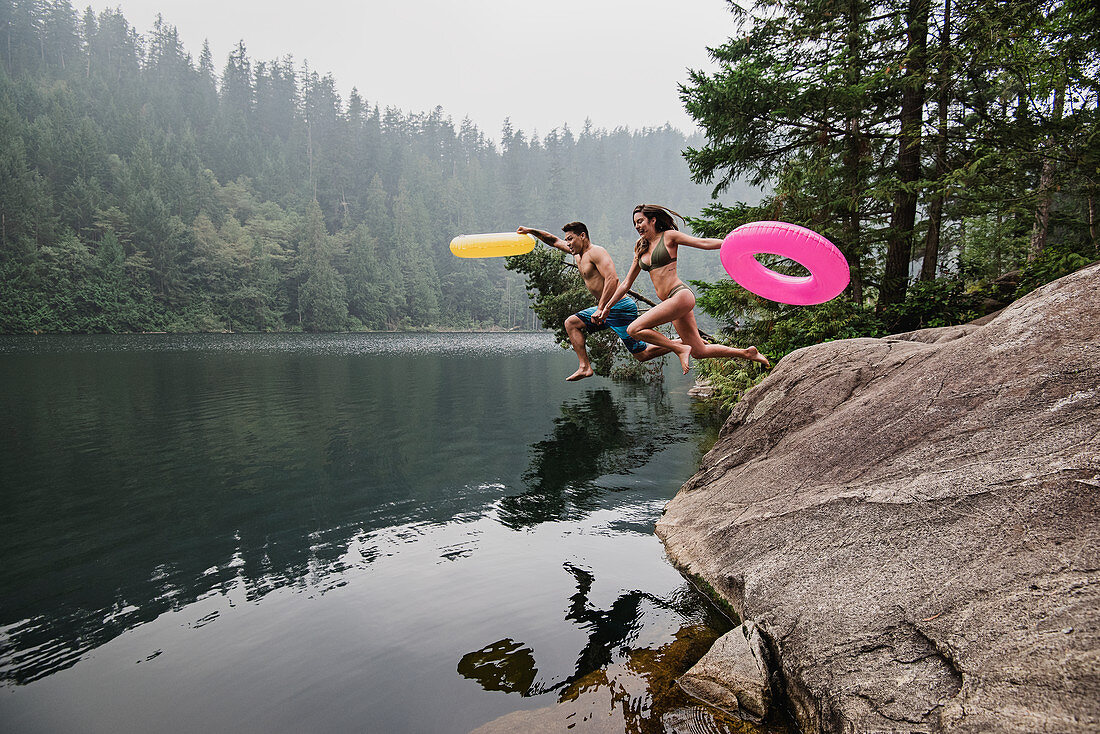 Playful couple jumping into lake, Canada