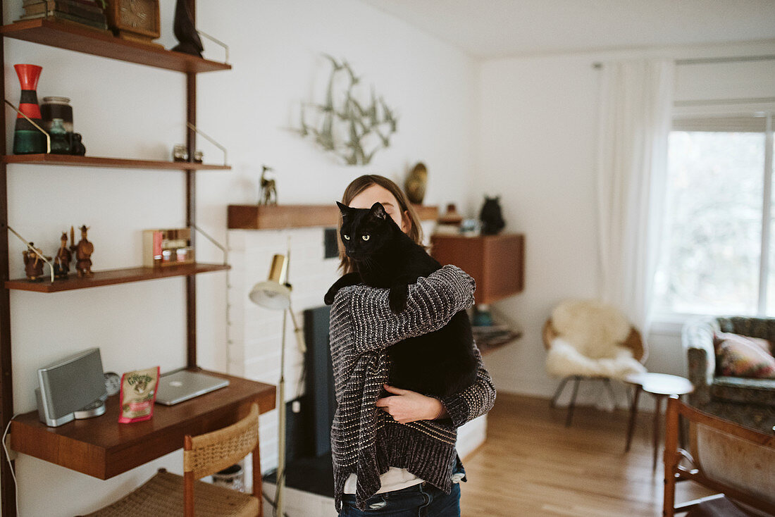 Girl holding black cat in living room