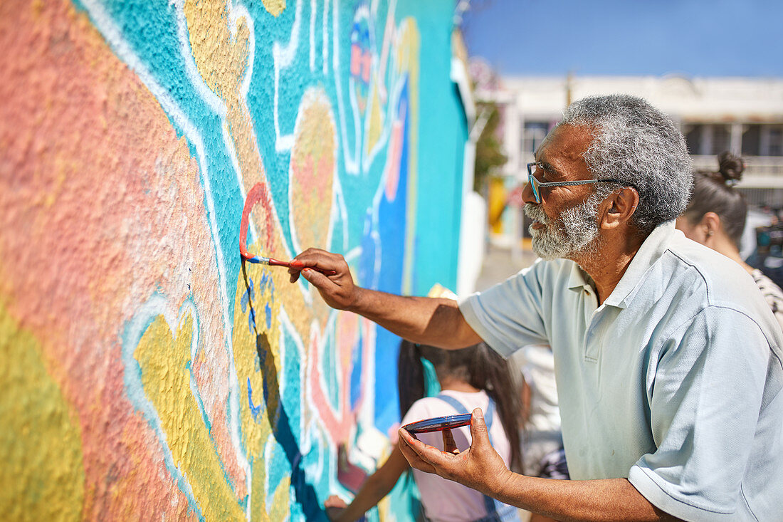 Senior male volunteer painting vibrant mural on wall