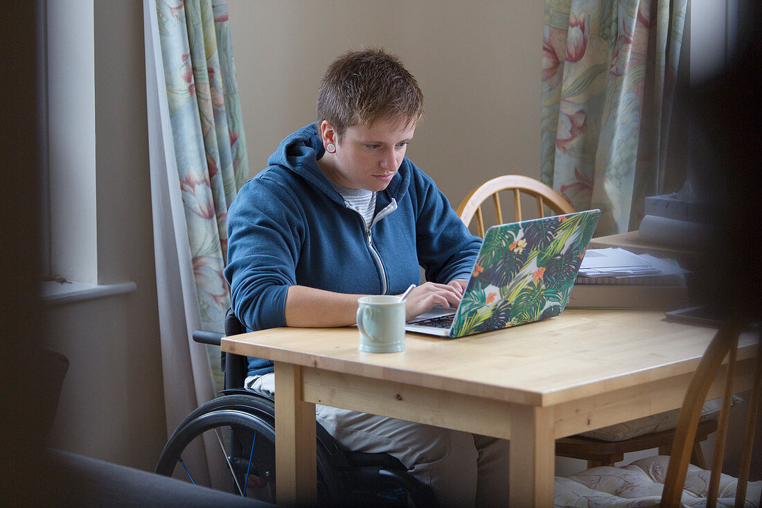 Focused woman in wheelchair using laptop