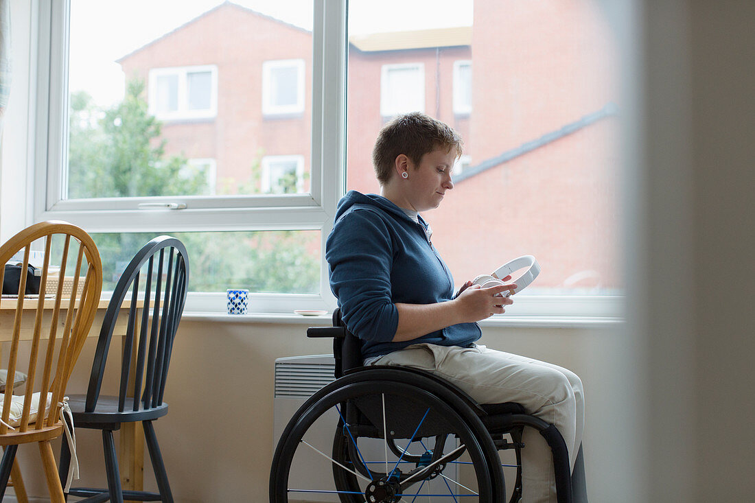 Young woman in wheelchair with headphones at window