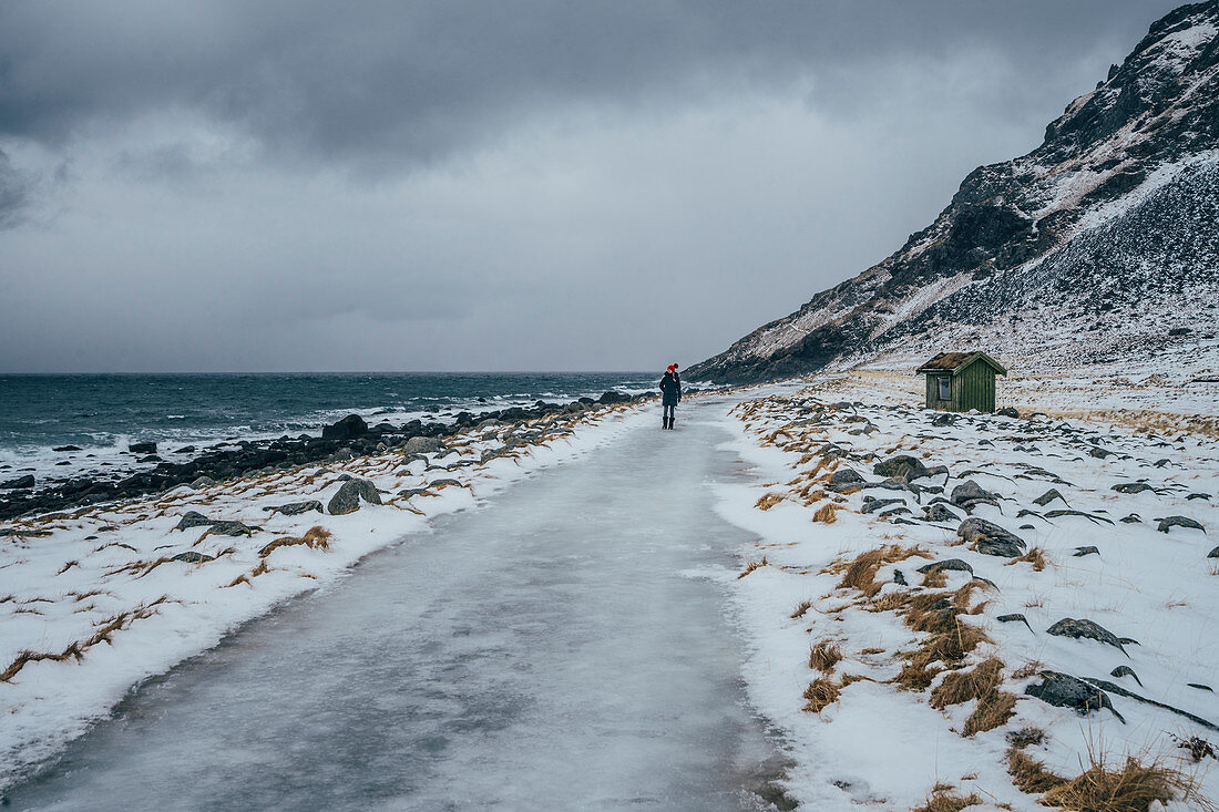 Woman walking along icy beach, Lofoten Islands, Norway
