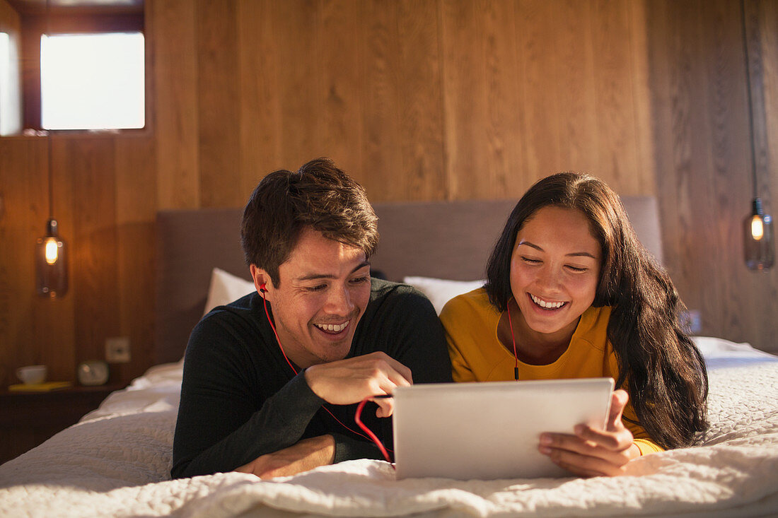 Happy young couple sharing digital tablet on bed