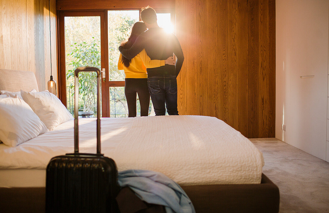 Couple with suitcase hugging in bedroom