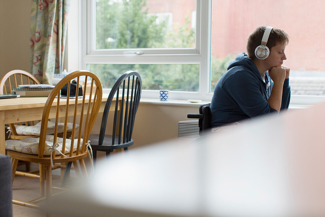 Serene woman in wheelchair listening to music at window