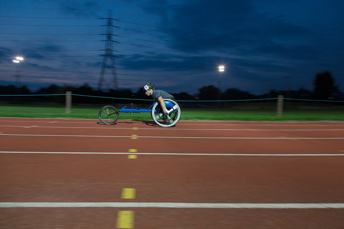 Young paraplegic athlete in wheelchair race at night