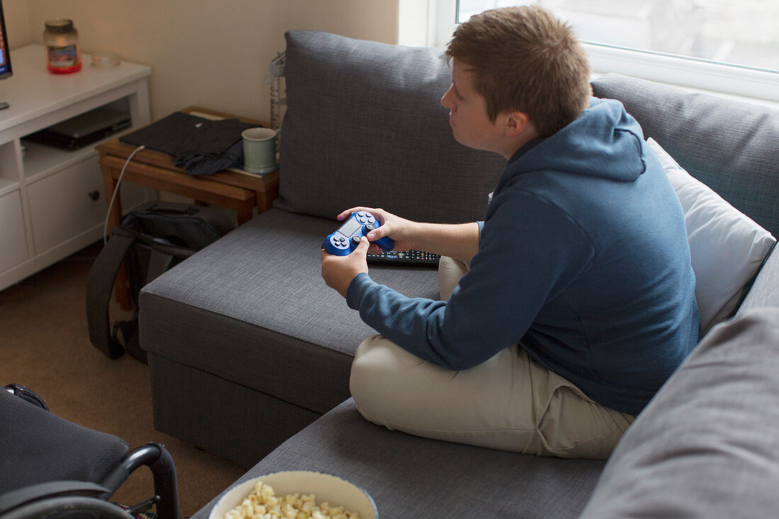 Young woman playing video game on sofa next to wheelchair