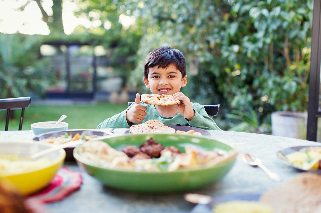 Portrait boy eating naan bread at patio table