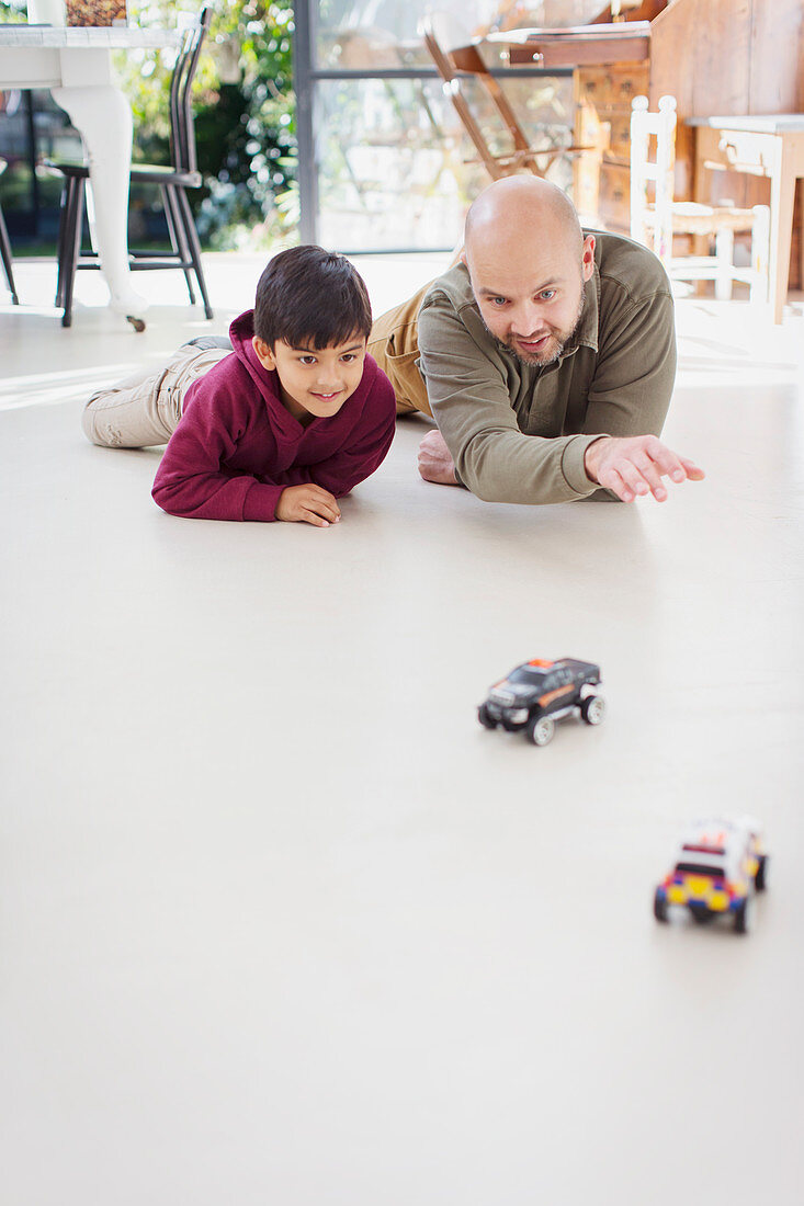 Father and son playing with toy cars on floor