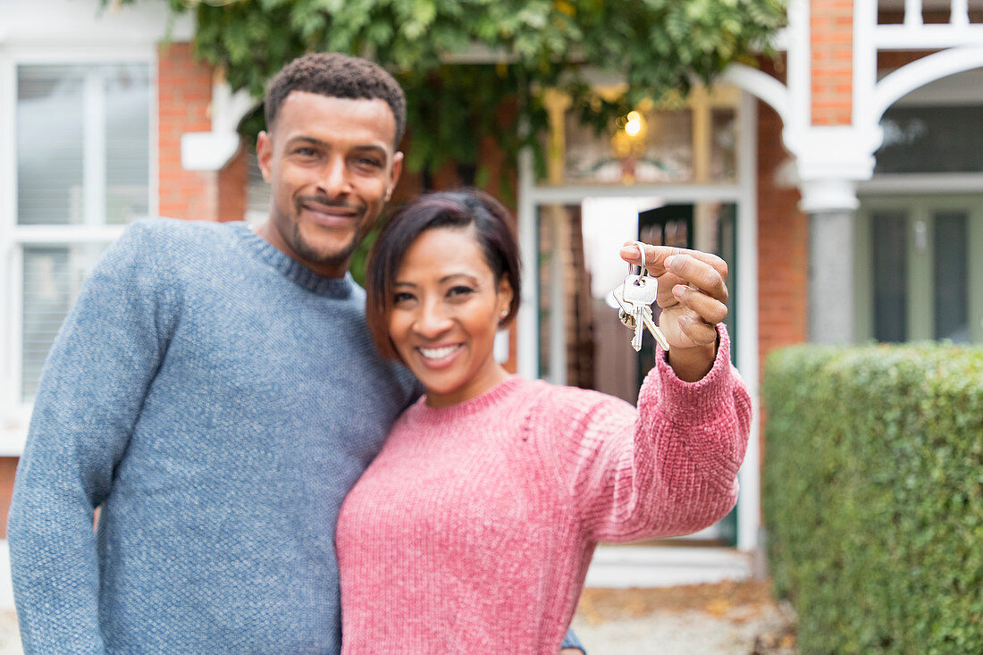 Portrait happy couple with house keys outside new house