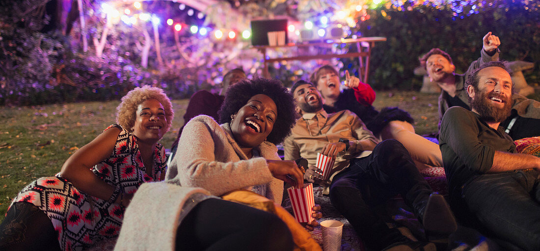 Laughing friends watching movie in backyard