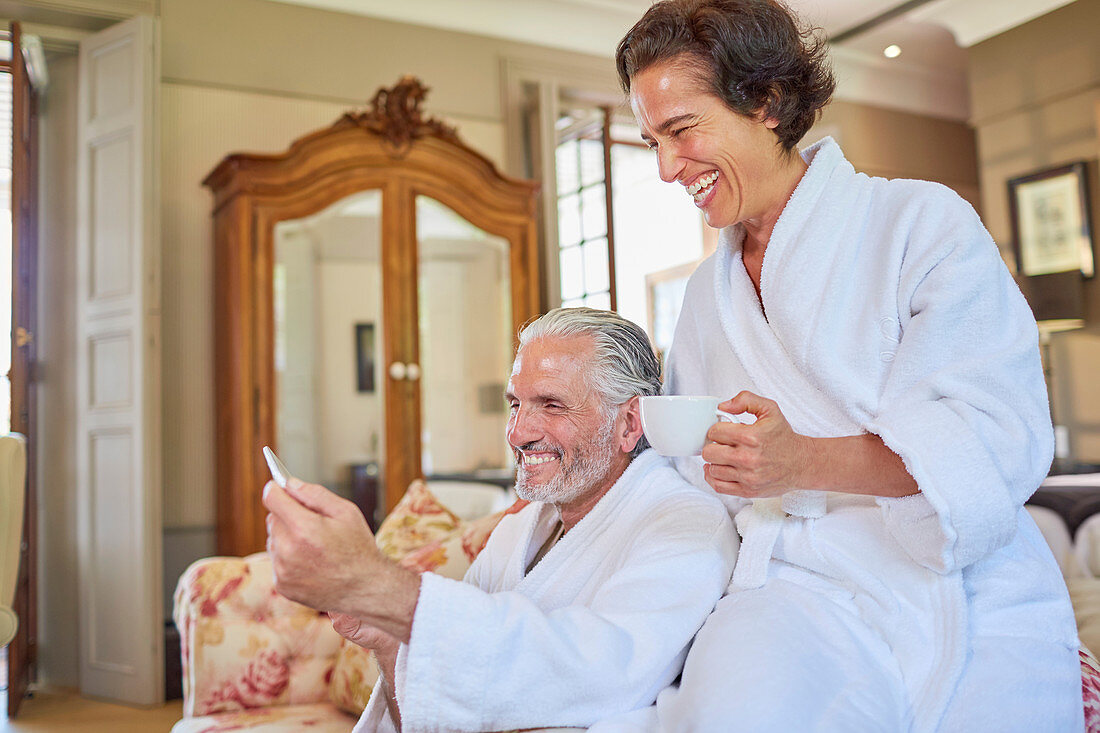 Happy mature couple in spa bathrobes drinking coffee