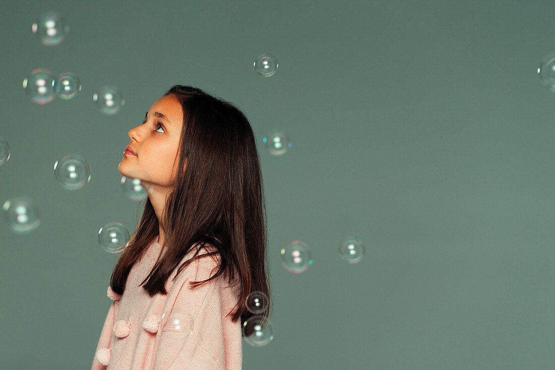 Serene, curious girl watching falling bubbles
