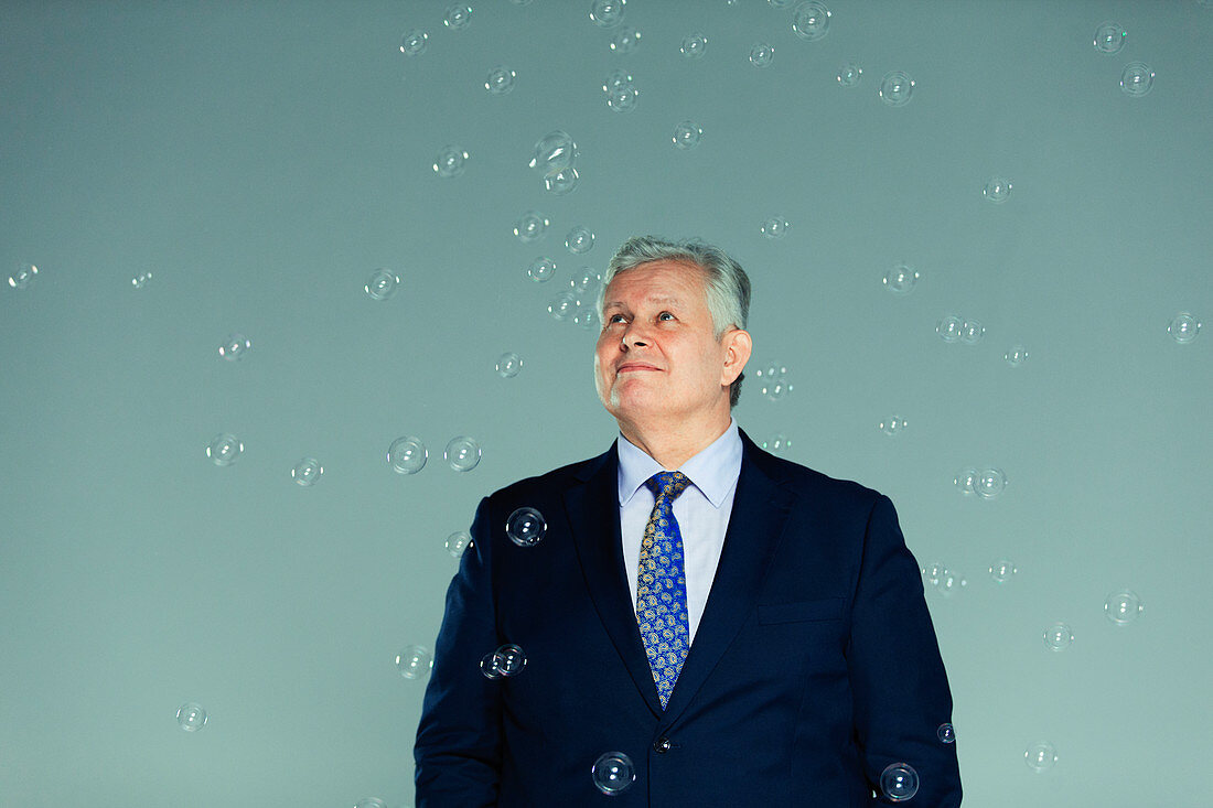 Smiling, curious businessman watching falling bubbles