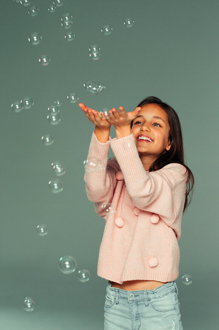 Smiling, carefree girl playing with falling bubbles