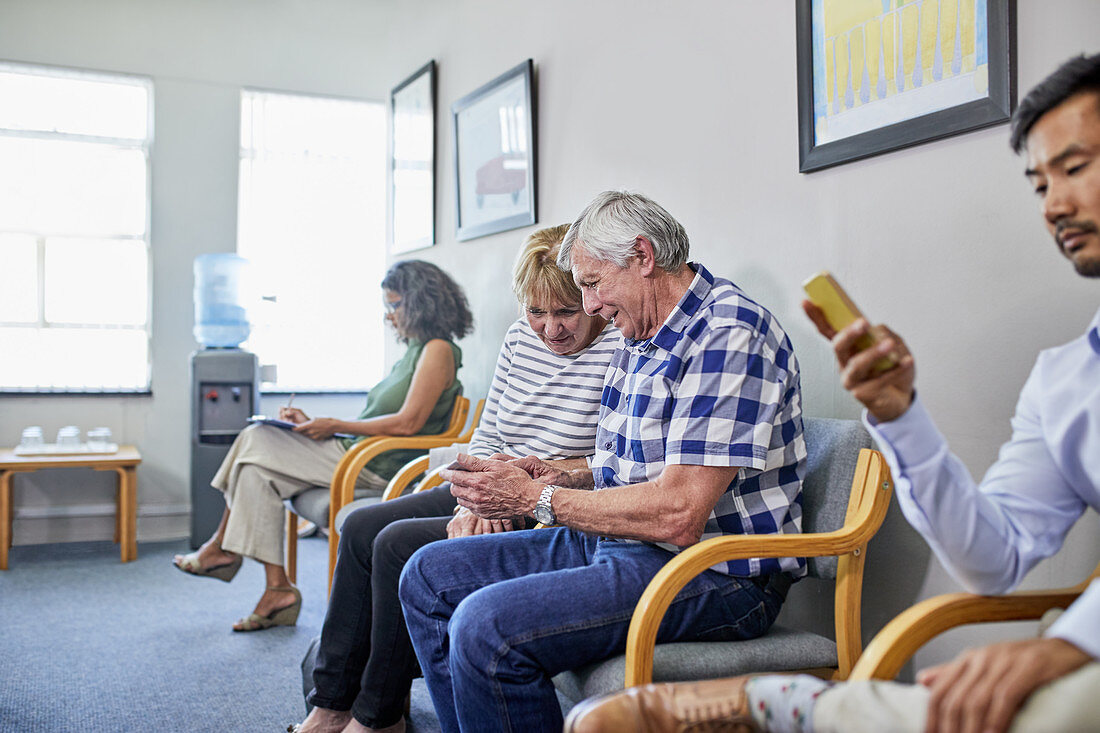 Senior couple using smart phone in clinic waiting room