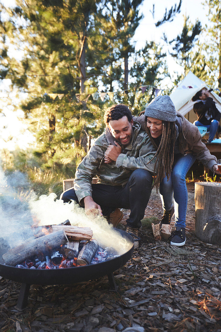 Happy couple tending to campfire at campsite in woods