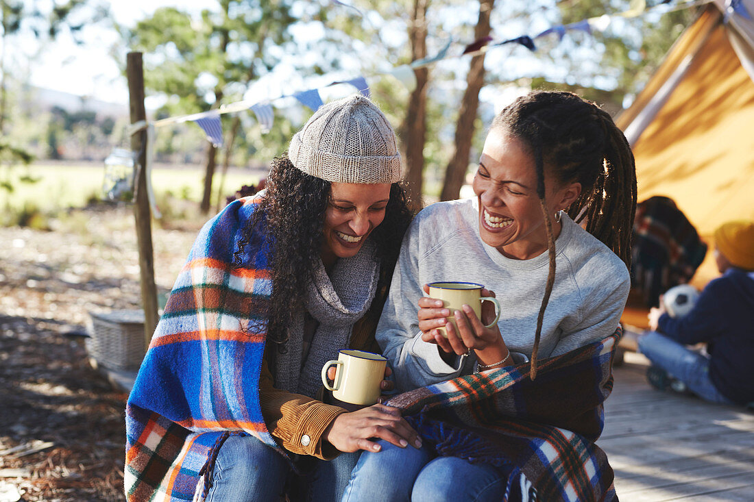 Lesbian couple laughing, drinking coffee at campsite