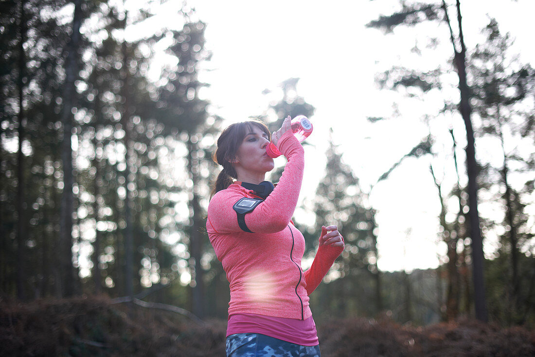 Female runner drinking from water bottle in woods