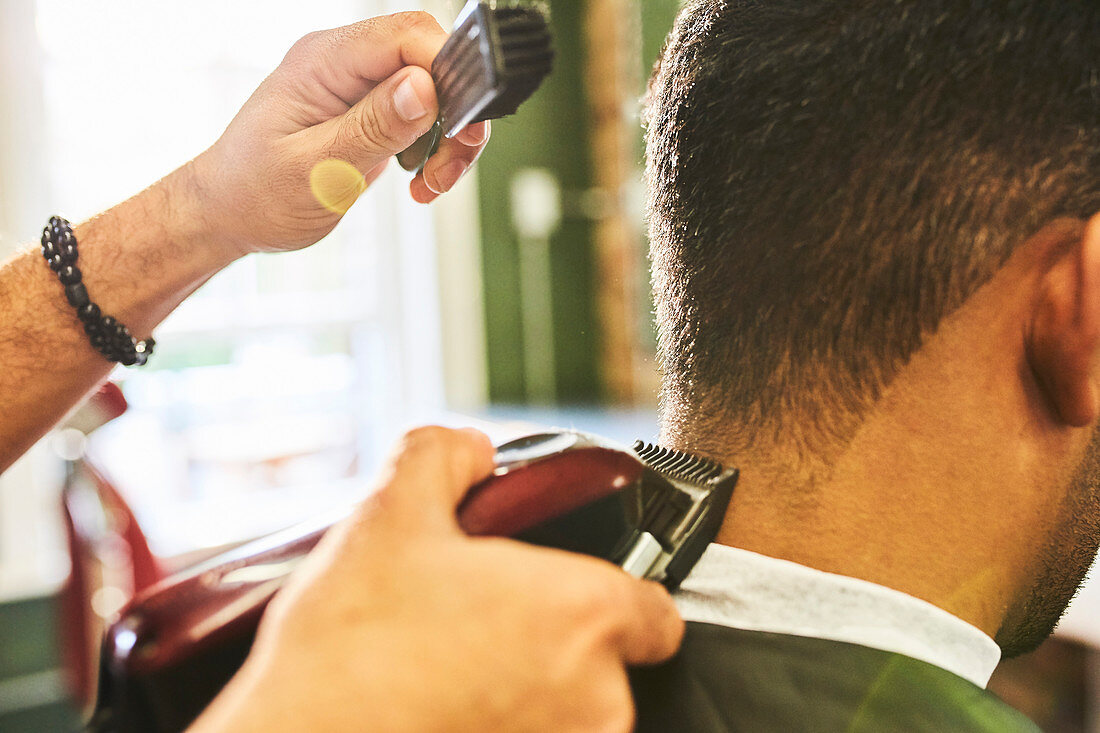 Close up male barber using trimmer on hair of customer